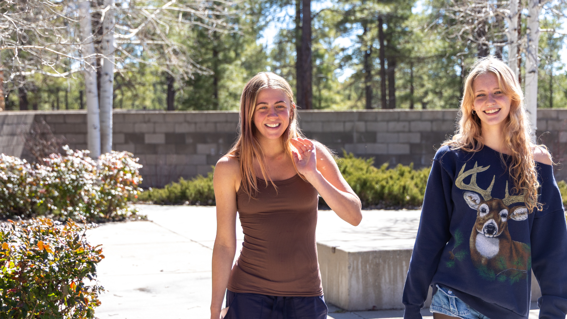 Two students walk across Coconino Community College's Lone Tree Campus on a sunny day, surrounded by trees, landscaping, and outdoor gathering spaces.